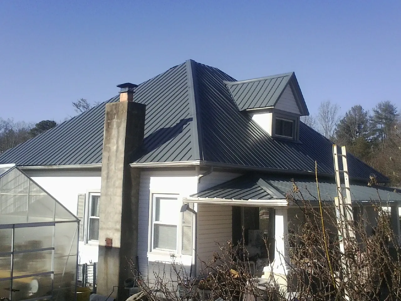 Dark blue standing seam metal roof on a white farmhouse with dormer — Slate & Tile Roof Repair by Roofing Brothers in Lake Park