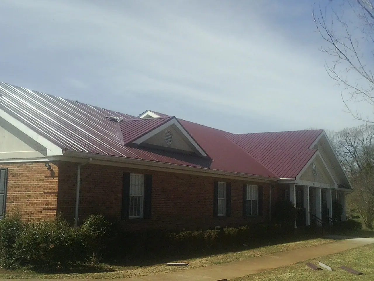 Red metal roof with gabled entries on a long brick building, from a Hail Damage Roof Repair job in Lake Park