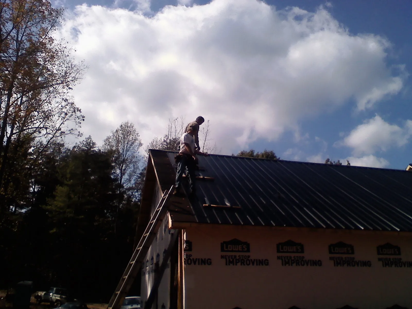 Roofer fastening dark metal panels high against a cloudy sky, from a Roof Inspection job in Lake Park