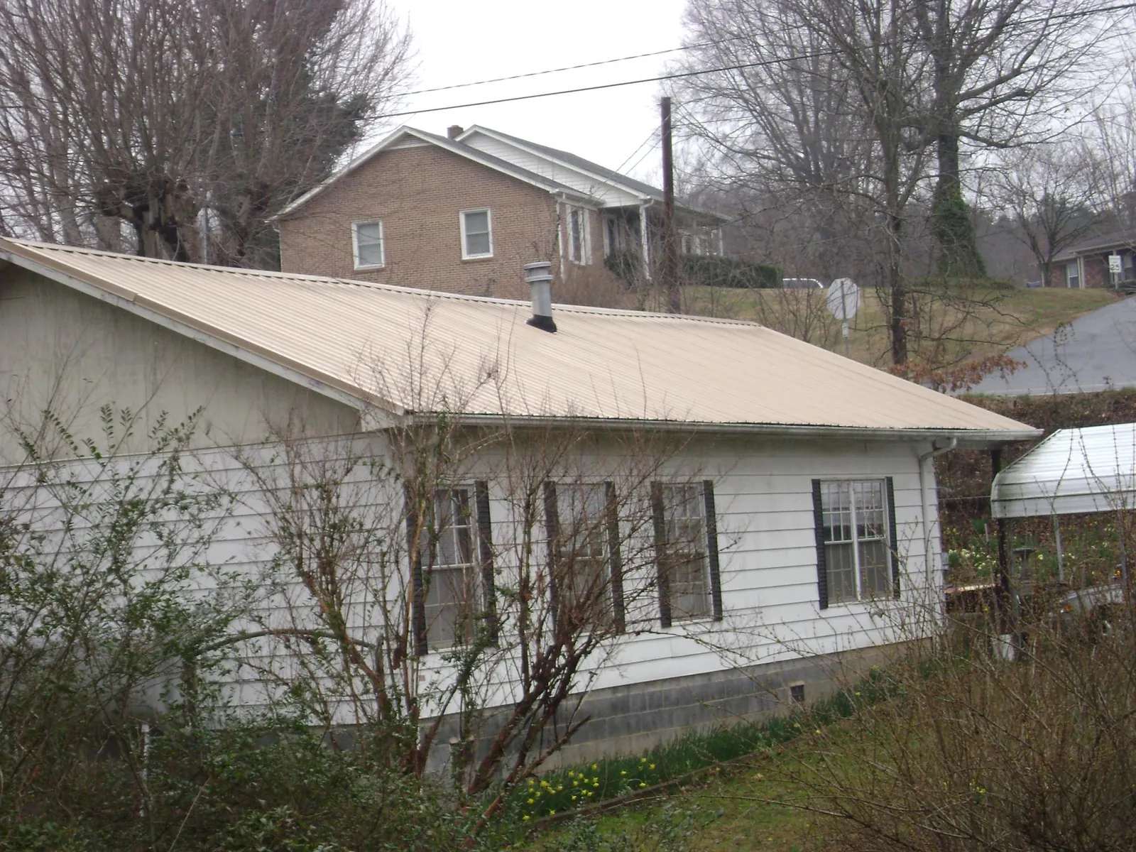 Tan metal roof on a white sided house set into a hillside — Commercial Roofing by Roofing Brothers in Lake Park